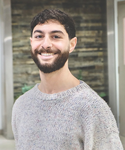 Man with beard in gray sweater standing in front of wall